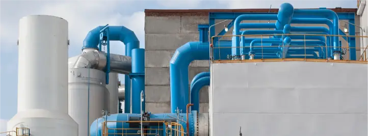 Industrial facility with bright blue interconnected pipes and large vertical tanks against a pale sky.