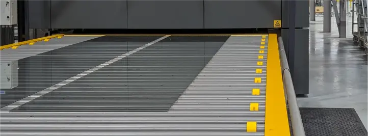 Industrial loading dock with a metal roller conveyor and yellow safety edge guides.