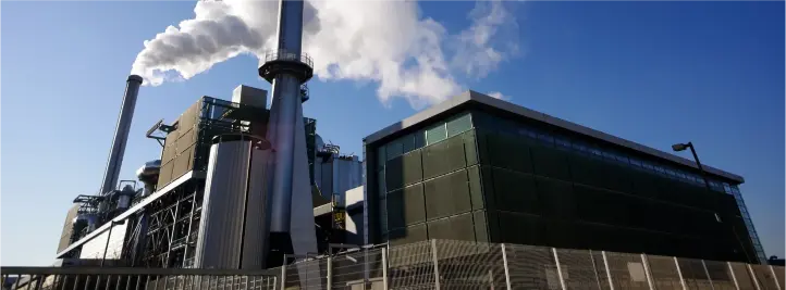 Industrial power plant with tall smokestacks emitting white steam behind a fenced area under a blue sky.
