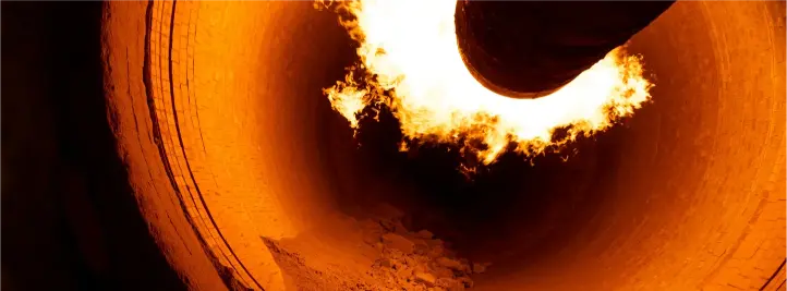 Inside a brick-walled furnace, an intense orange flame erupts from the circular opening.