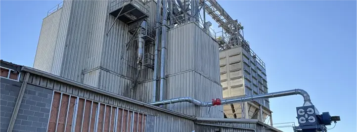 Industrial plant with tall metal silos, staircases, and network of pipes against a blue sky