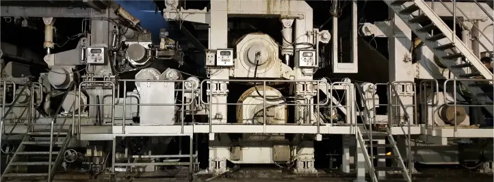 Heavy industrial plant with large machinery, catwalks, and metal stairs visible in a dense factory setup.