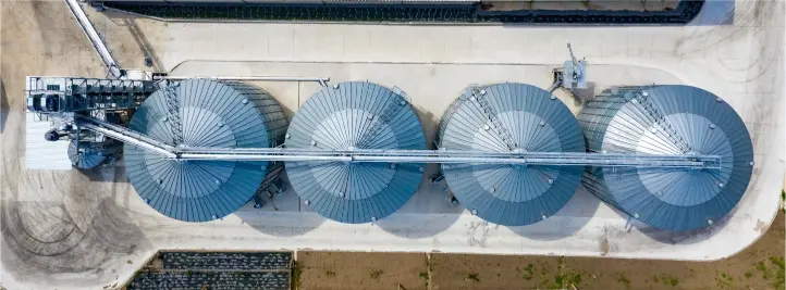 Aerial view of four large circular industrial storage tanks connected by a central pipe on a concrete platform.