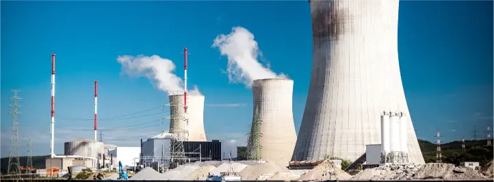Industrial power plant with tall cooling towers emitting steam against a clear blue sky.