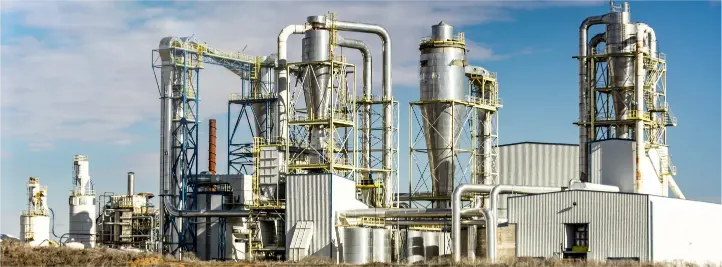 Industrial chemical processing plant with tall distillation columns and interconnected pipes under a blue sky.