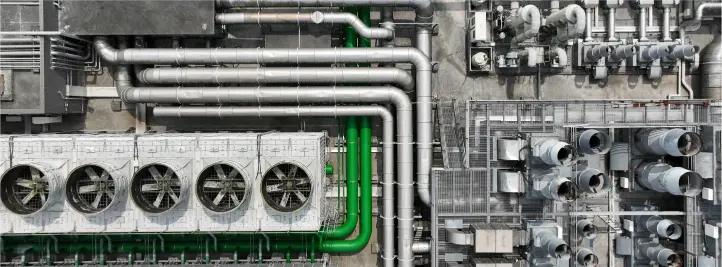 Aerial view of an industrial plant with many silver pipes and a bright green pipe running through the center.