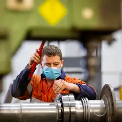 Industrial worker in orange coveralls wearing a blue mask tightens a pipe flange with a red tool in an industrial setting,
