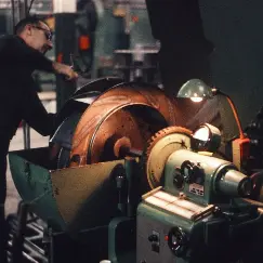 Industrial workshop: technician operating a large metal lathe with a copper workpiece