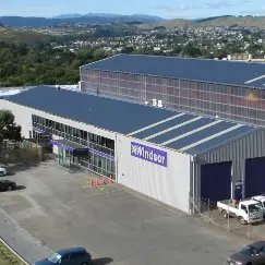 Industrial warehouse with a blue roof and a purple Windsor sign, parking spaces in front and a loading bay on the side.