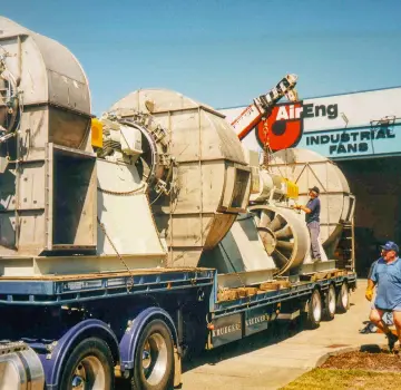 Oversized industrial ventilation fans on a flatbed trailer at an AirEng Industrial Fans site, with workers nearby.