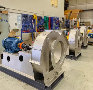 Industrial workshop with large stainless steel centrifugal pump/blower units mounted on blue bases and connected to blue motors.