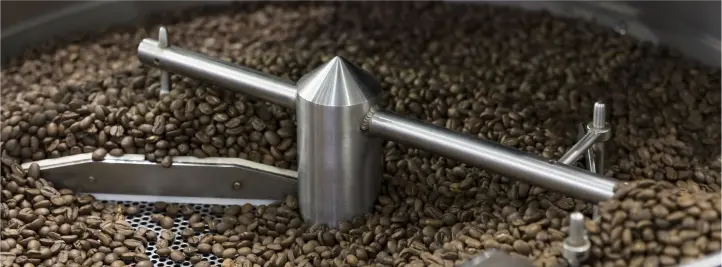 Industrial coffee roasting drum agitator spinning through roasted beans in a metal roasting system.