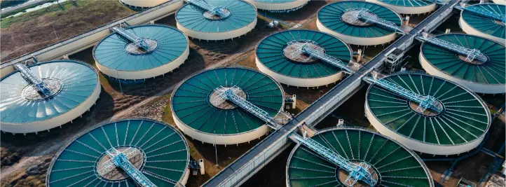 Aerial view of multiple circular wastewater treatment clarifier tanks with green covers and connecting pipes.