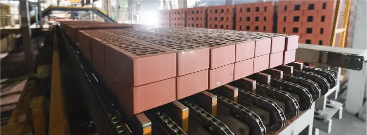 Stack of red clay bricks on a conveyor belt in a brick manufacturing plant.