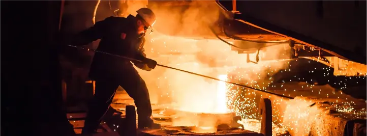 Blacksmith in a furnace-lit forge, wielding a long rod to shape glowing molten metal as sparks fly nearby, wearing a helmet.