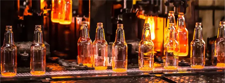 Row of empty glass bottles on a bottling conveyor with an orange-hot furnace glow in the background.