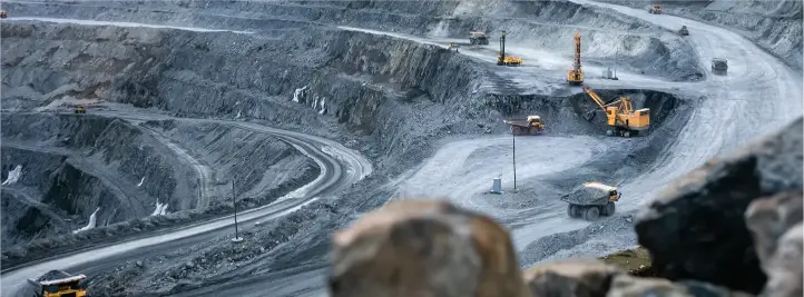Open-pit mining site with terraced benches, winding roads, and yellow excavators and trucks at multiple levels.