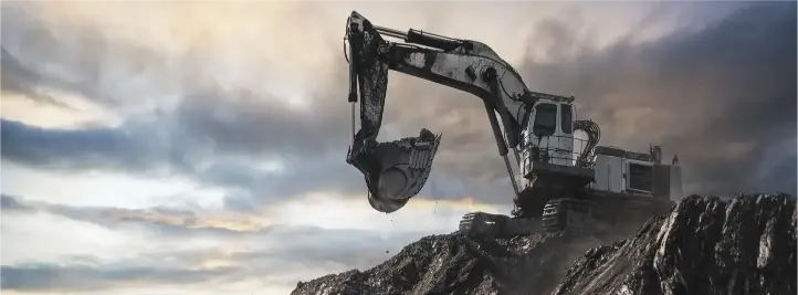 Heavy excavator on a rocky slope at a quarry, bucket raised as it digs under a cloudy sky.