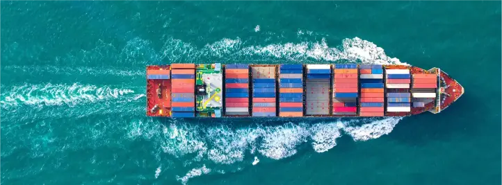 Aerial view of a cargo ship carrying stacked colorful shipping containers moving through turquoise sea. (top-down)
