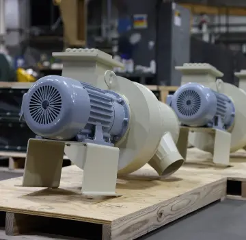 Two industrial centrifugal pumps with gray motors on wooden pallets in a factory.