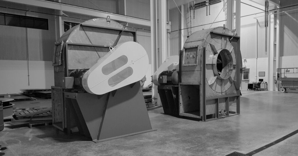Industrial factory interior with two large cylindrical processing machines and motors on a concrete floor.